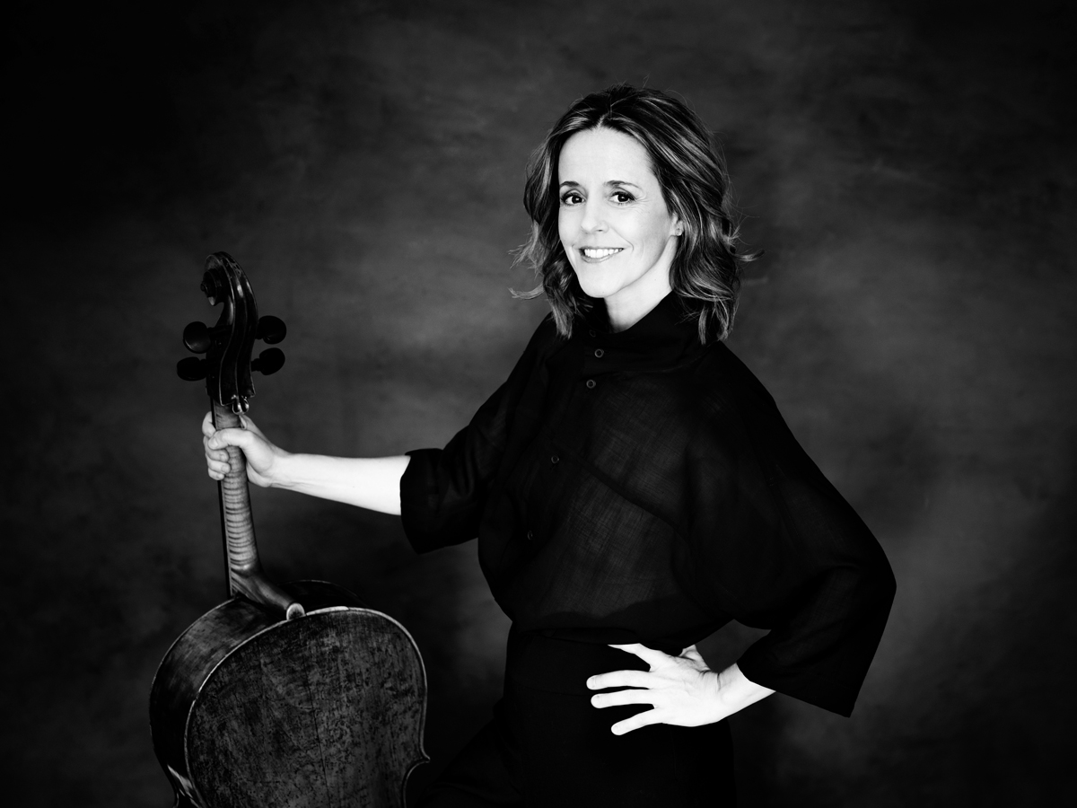 Schwarz-weiss Aufnahme von Sol Gabetta, welche ihr Cello hält und lächelnd in die Kamera schaut.